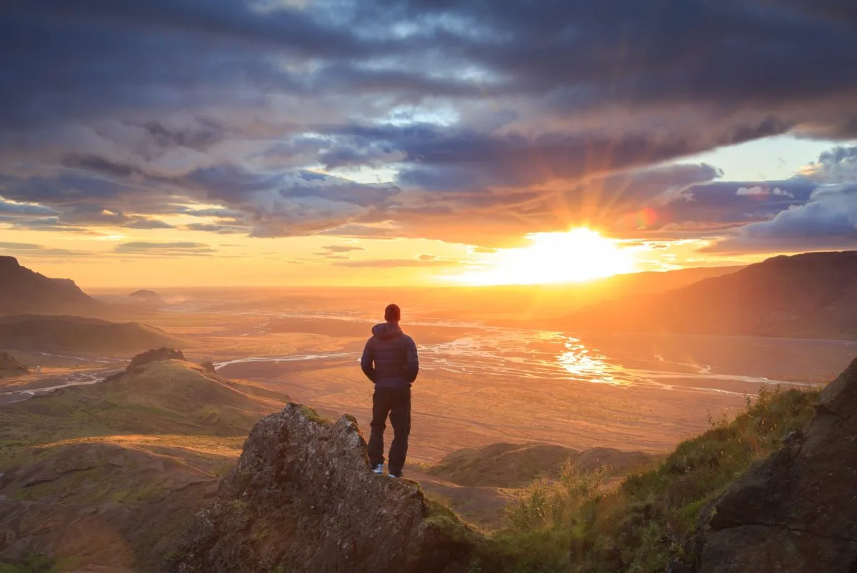 Man standing on a ledge of a mountain, enjoying the sunset over a river valley in Thorsmork, Iceland.